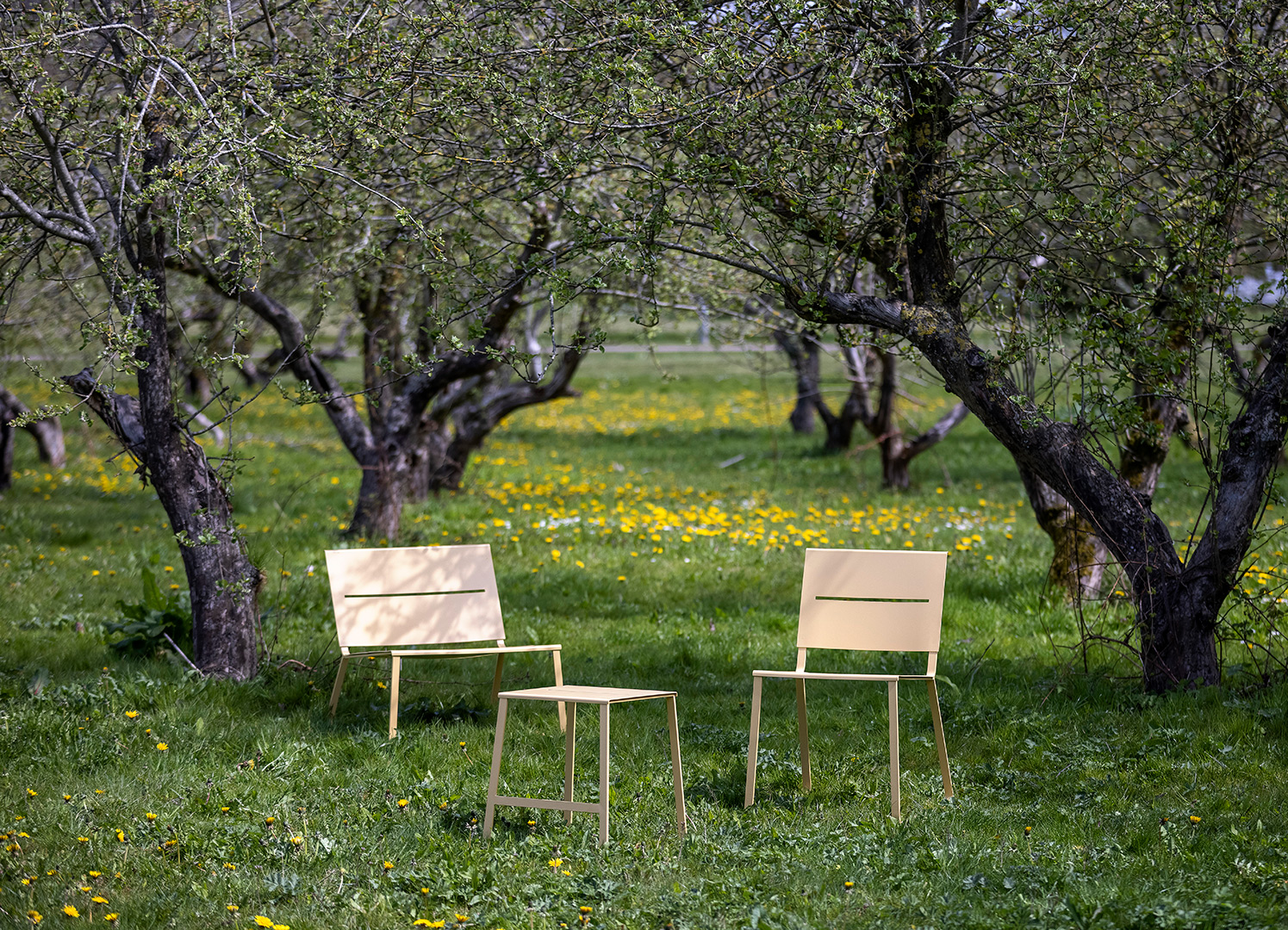 Loungestol, stol och pall i stål står under äppelträd